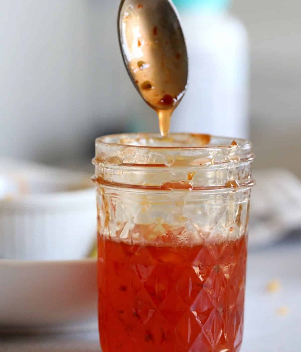 Asian Thai chili sauce dripping from a spoon with red pepper flakes