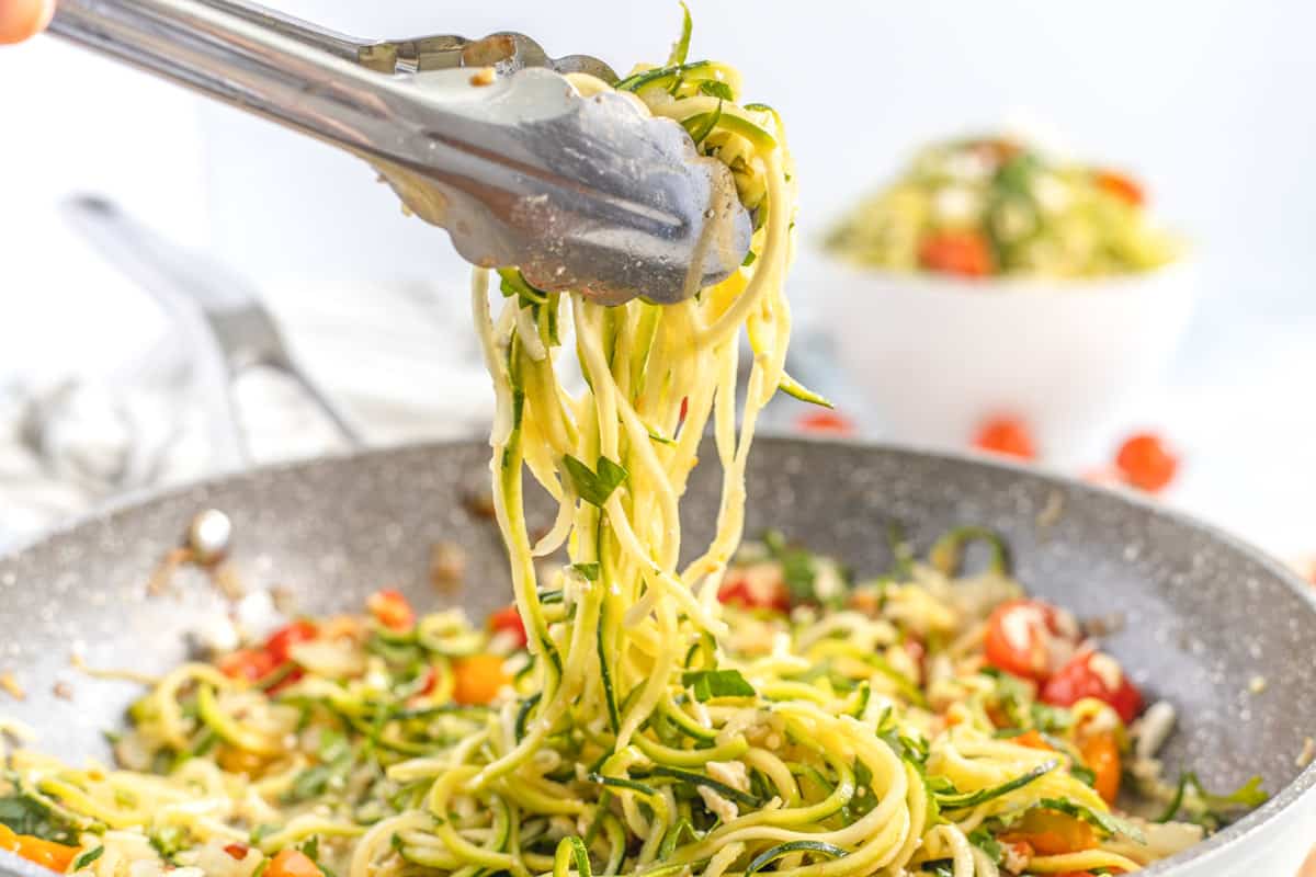 tongs lifting zucchini pasta from a frying pan