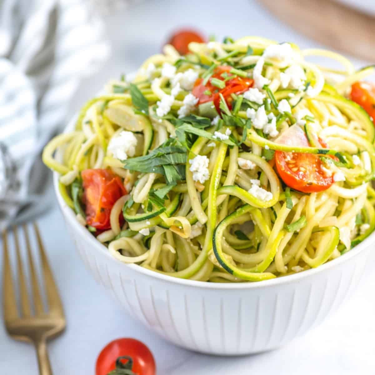 bowl of zucchini feta pasta with zoodle spirals, cherry tomatoes, and fresh parsley