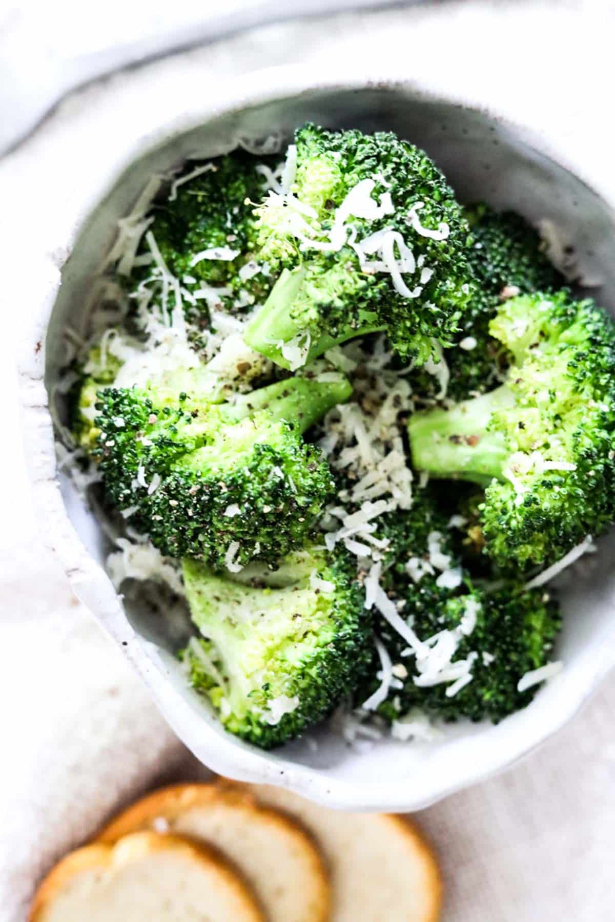 broccoli in a bowl with shaved parmesan cheese and pepper on top