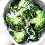 broccoli florets in a bowl with shaved parmesan cheese topping and pepper