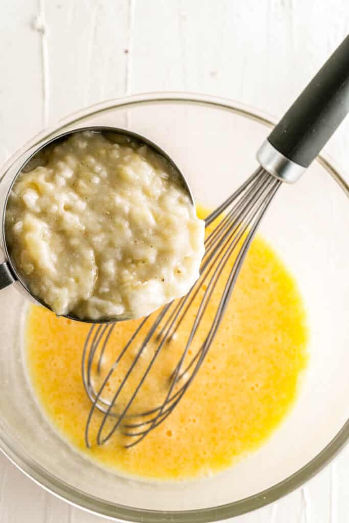 adding mashed banana to a bowl with a whisk