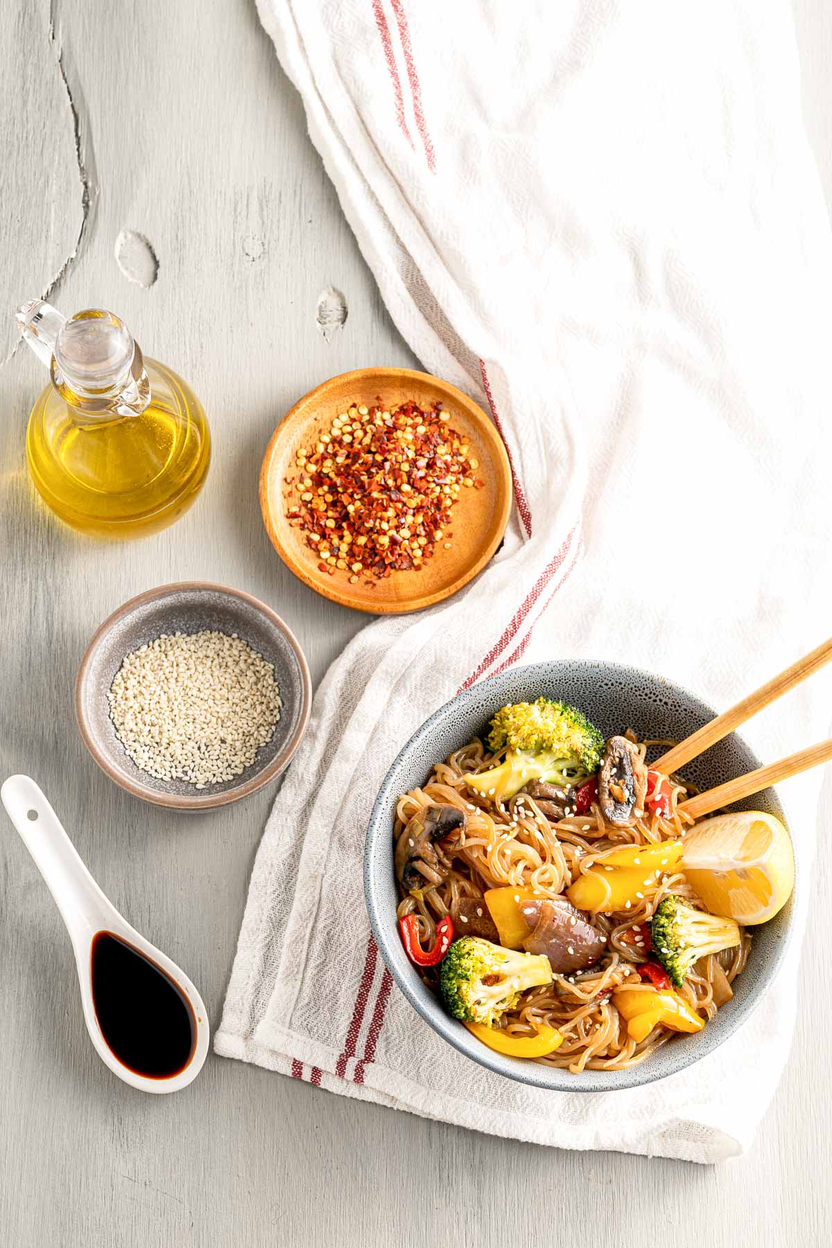 bowl of stir fry with ingredients on a table with a tablecloth, oil, noodles, and soy sauce