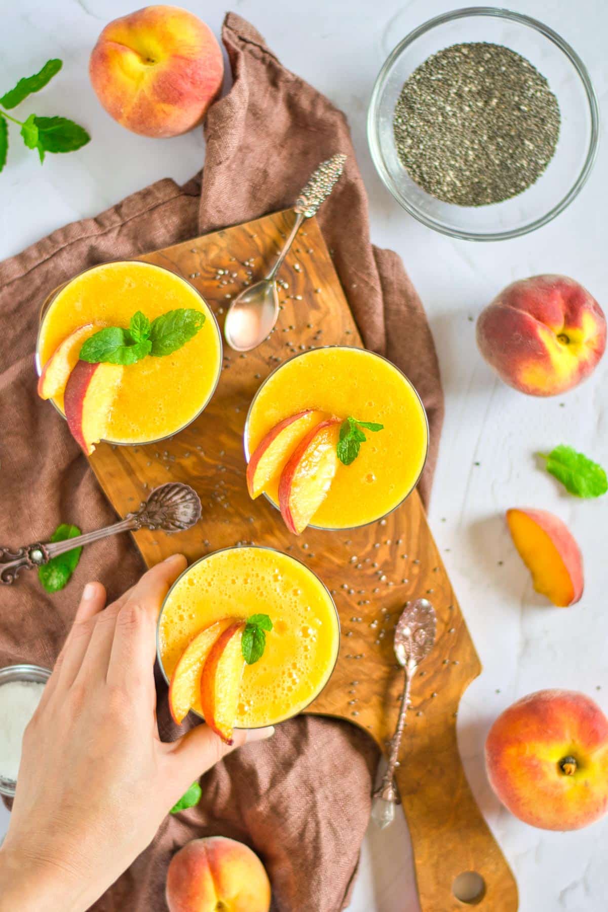 three chia peach pudding cups on a wooden board with peaches all around the table