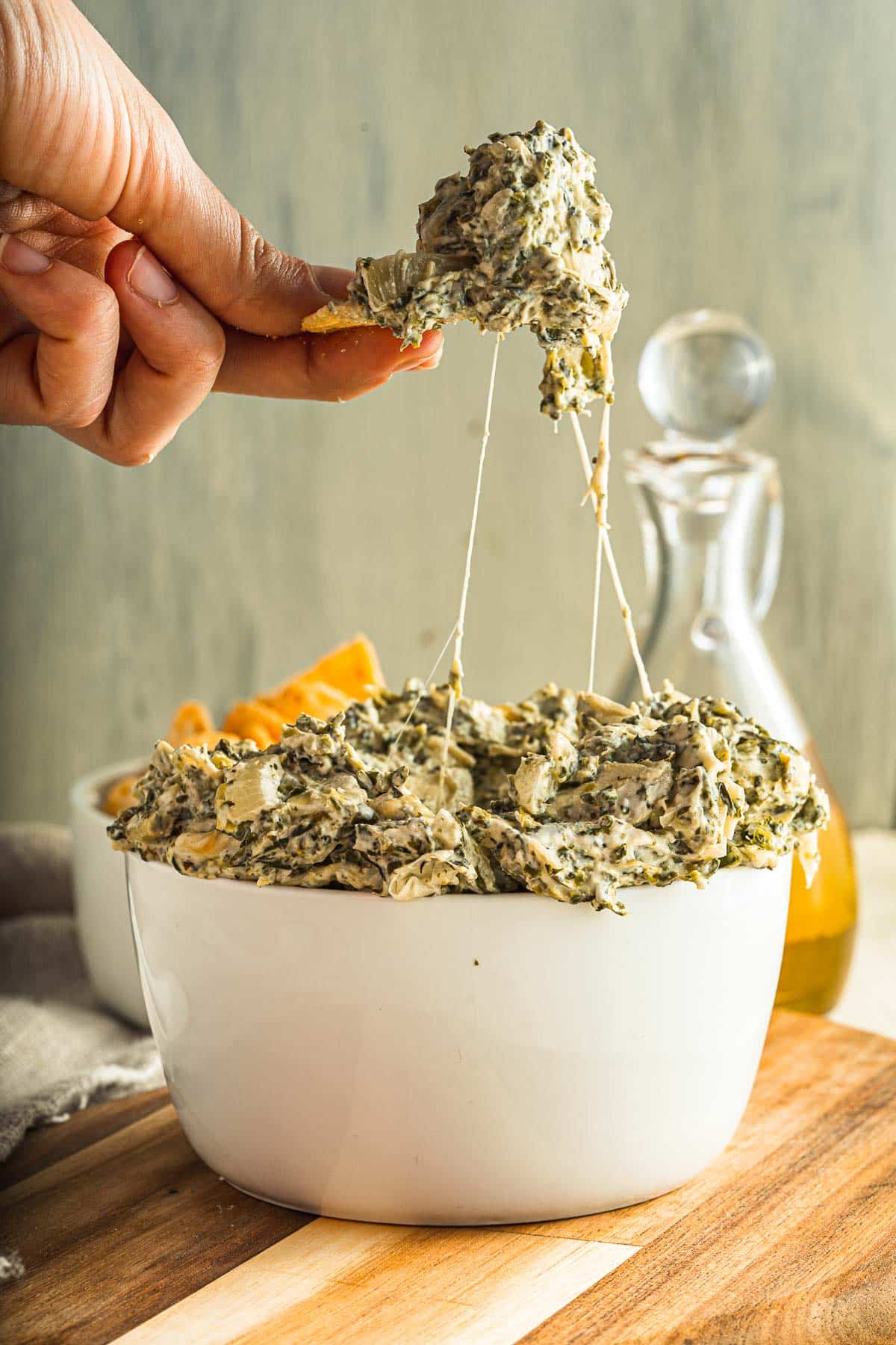 spinach artichoke dip being scooped up from a bowl with strings of cheese