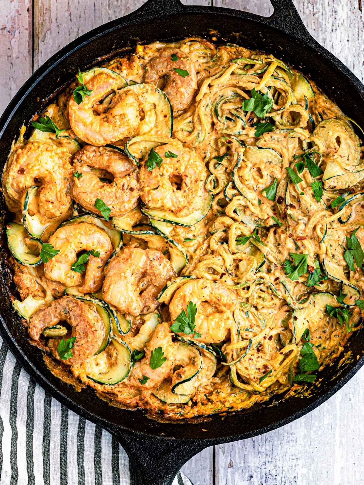 Mediterranean shrimp with zucchini spirals in a cast iron skillet on a striped napkin