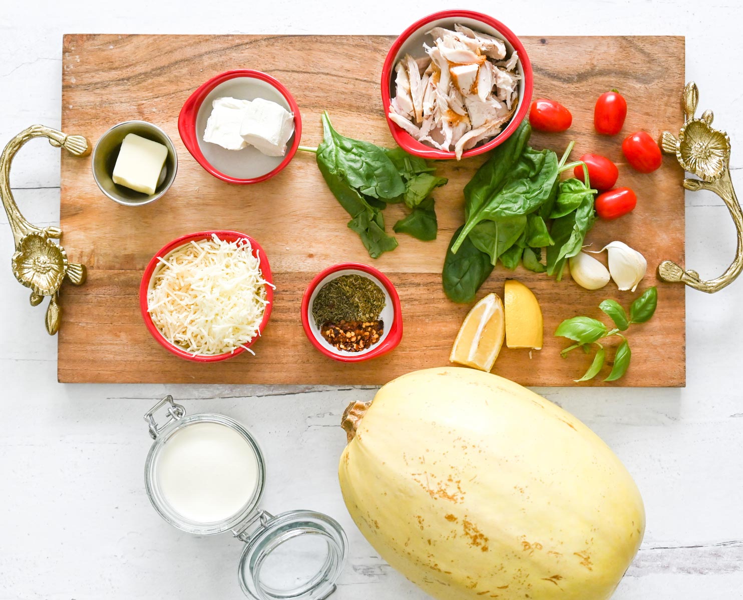ingredients on a table with a cutting board, including spaghetti squash, cheeses, tomatoes, spinach and garlic