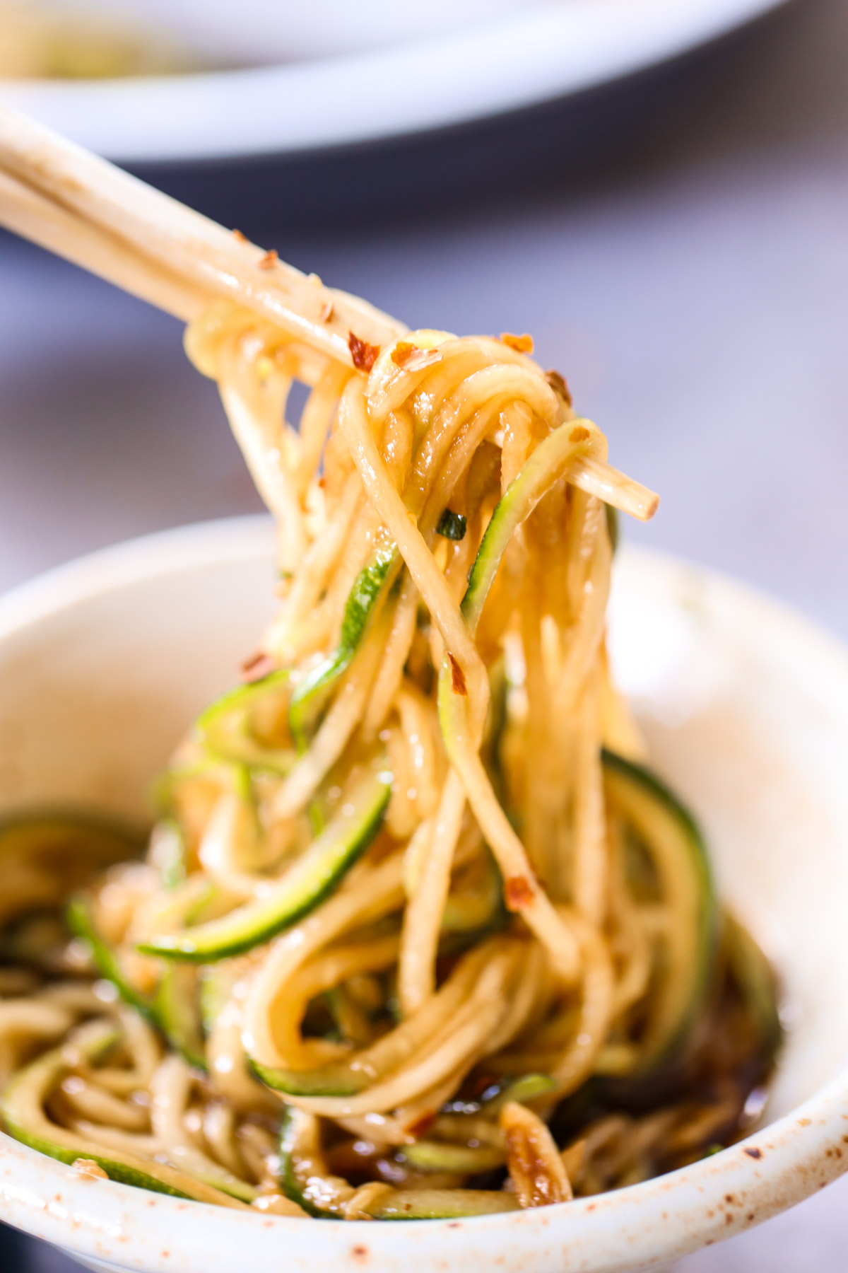 zoodle lo mein being lifted from a bowl with wooden chopsticks