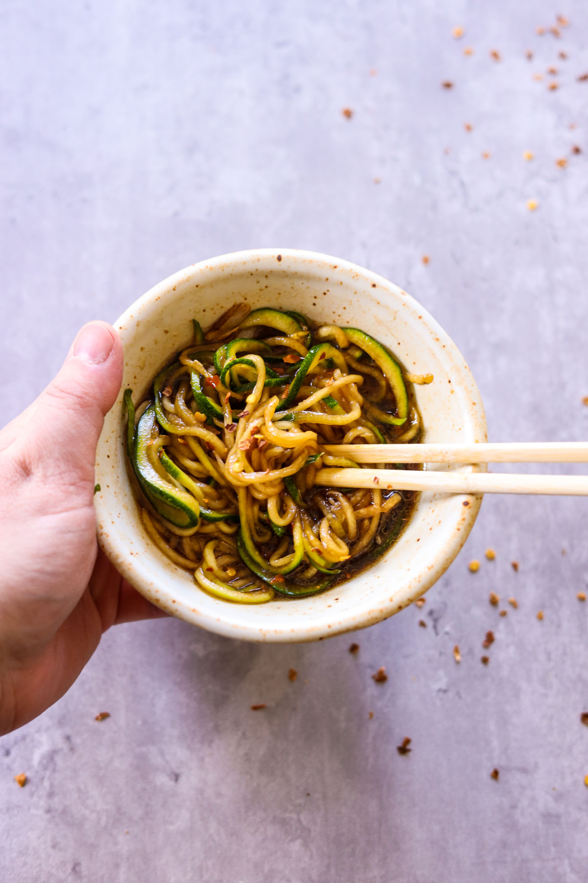 hand holding a bowl of zucchini lo mein stir fry noodles