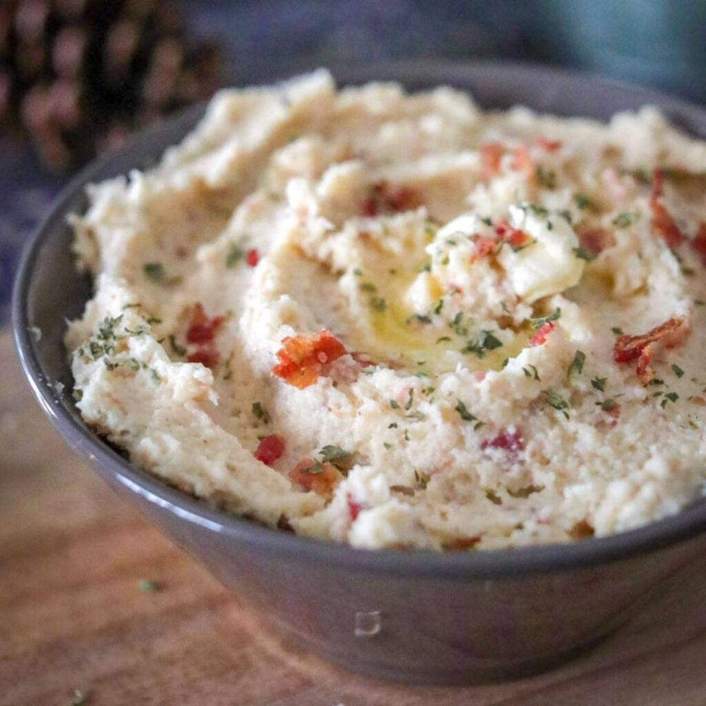 bowl of cauliflower mash with bacon bits, creamy butter and parsley