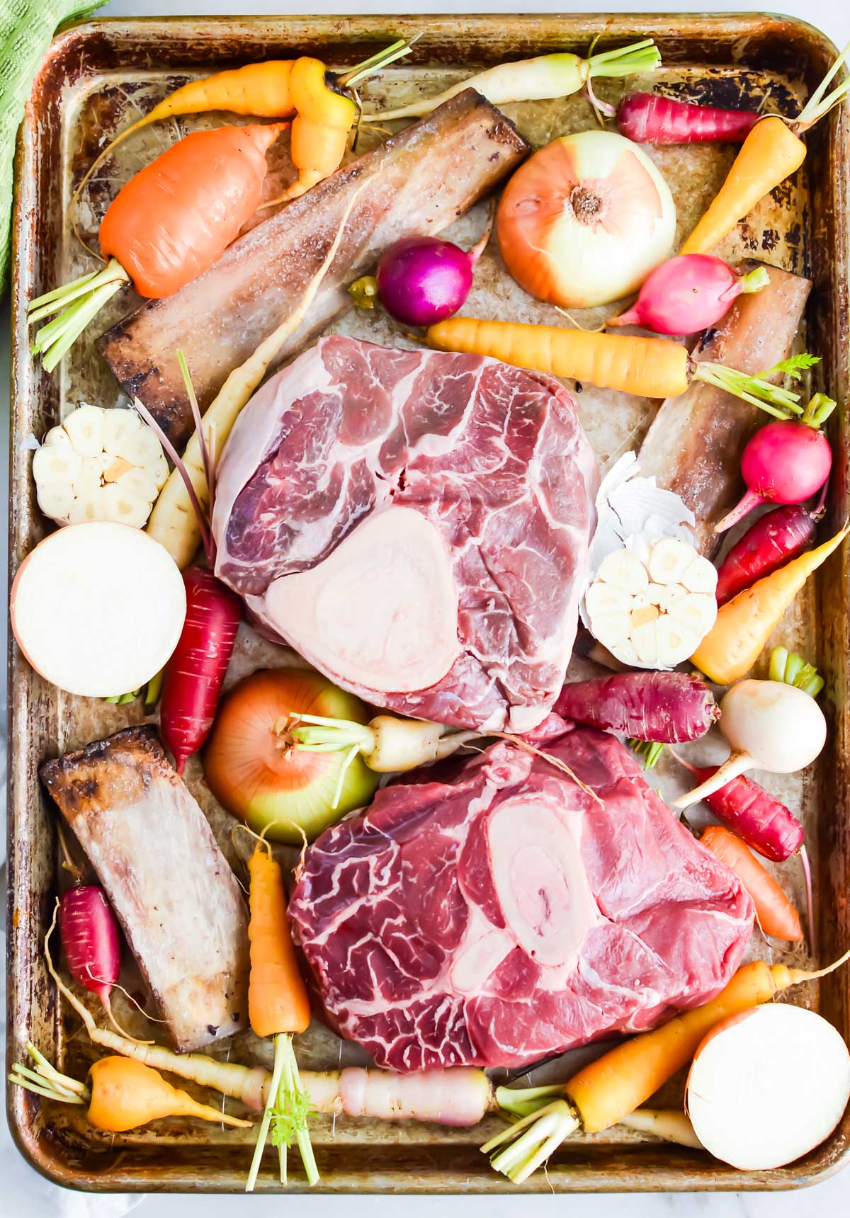bone broth ingredients with veggies on a baking sheet, including radishes, carrots, bones, onions and garlic