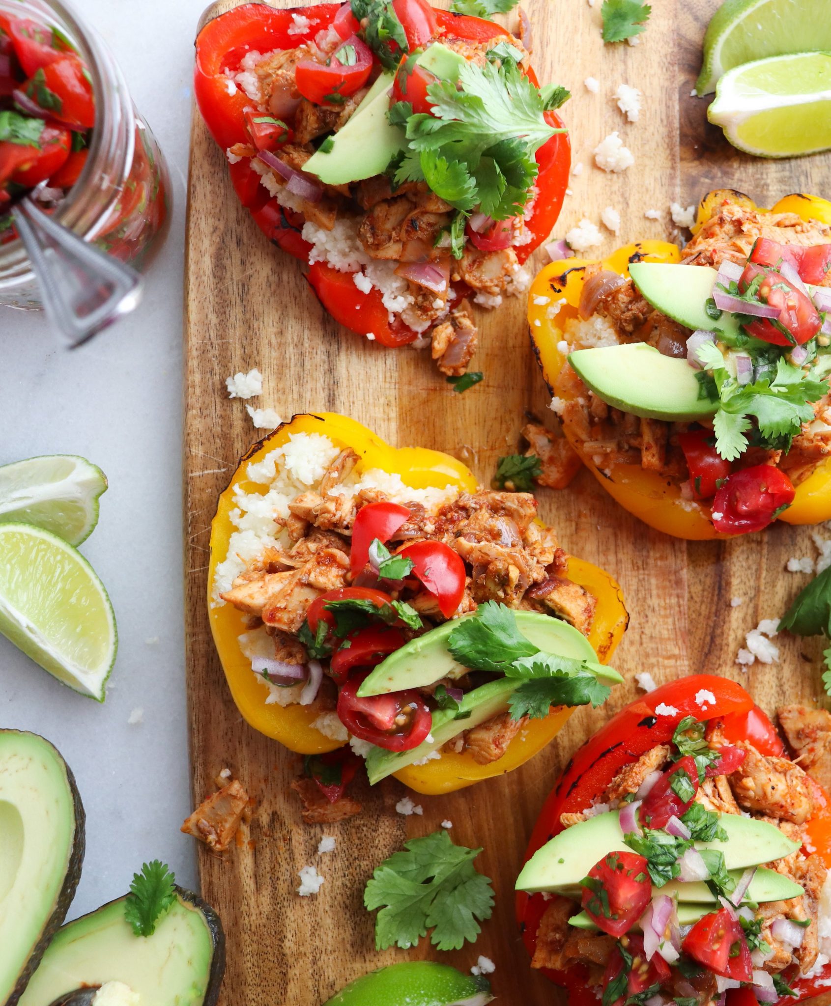 roasted stuffed bell pepper halves on a wooden cutting board garnished with avocado and tomatoes