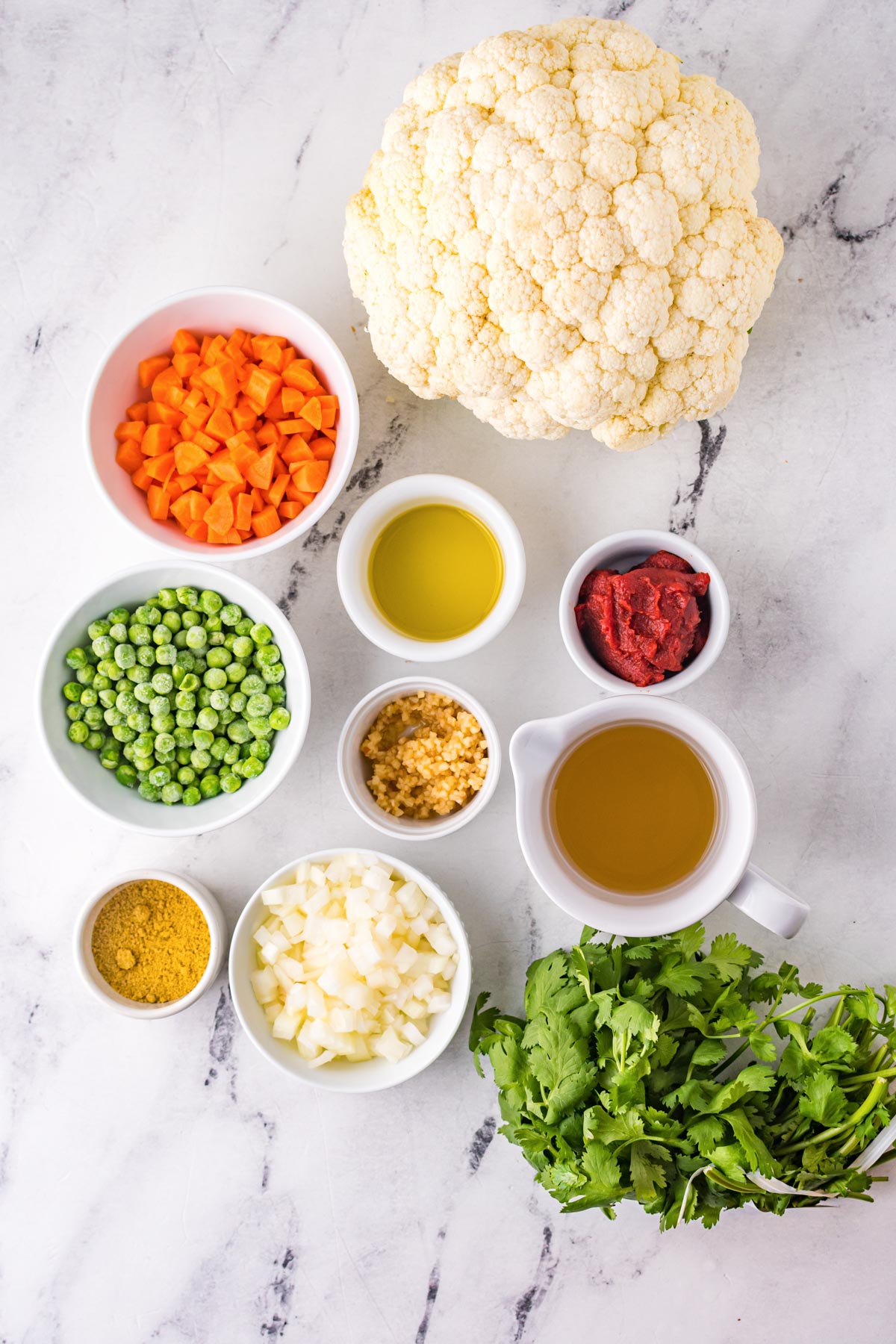ingredients for Mexican cauliflower rice, including cauliflower, peas, carrots, tomato paste, chicken broth, cilantro