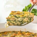 slice of frittata with mushrooms and spinach being lifted from a casserole dish