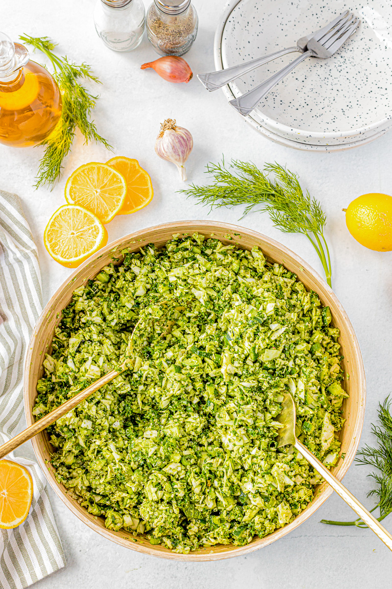 salad tongs in a large bowl with cabbage, kale, cucumber and salad dressing