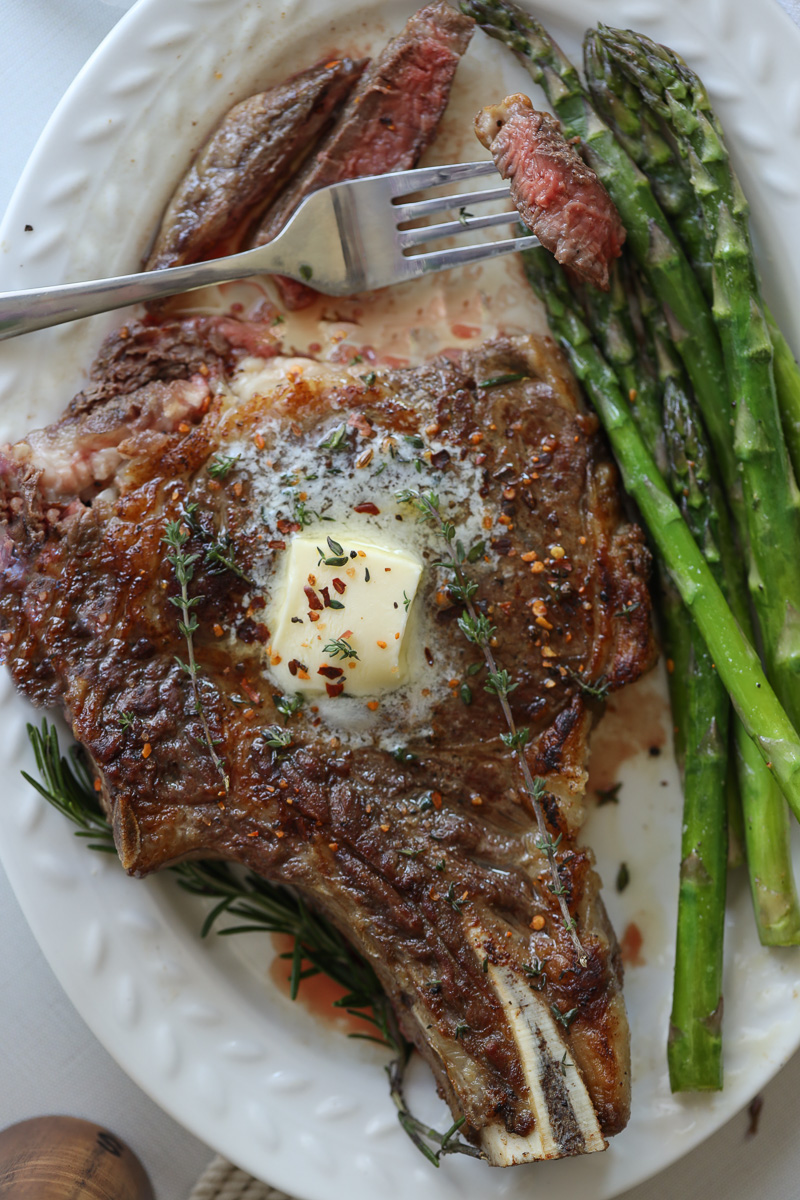 ribeye steak with butter on top and asparagus on the side