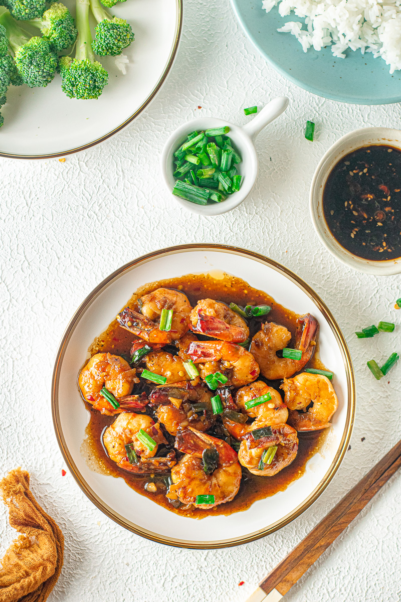 plate of sticky honey garlic shrimp next to scallions and soy sauce